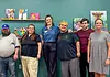 PRESS RELEASE: AutismOklahoma and Delta Dental debut video to ease dentist visit anxiety for people with autism Eight people pose for a group photo in an art studio with colorful paintings on a teal wall behind them.