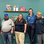 PRESS RELEASE: AutismOklahoma and Delta Dental debut video to ease dentist visit anxiety for people with autism Eight people pose for a group photo in an art studio with colorful paintings on a teal wall behind them.