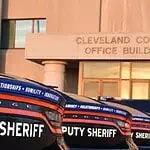 Cleveland County Sheriff resigns following embezzlement plea deal Row of black Dodge deputy sheriff patrol cars lined up in front of the Cleveland County Office Building exterior, displaying bold ‘DEPUTY SHERIFF’ lettering.