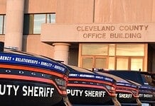 Row of black Dodge deputy sheriff patrol cars lined up in front of the Cleveland County Office Building exterior, displaying bold ‘DEPUTY SHERIFF’ lettering.