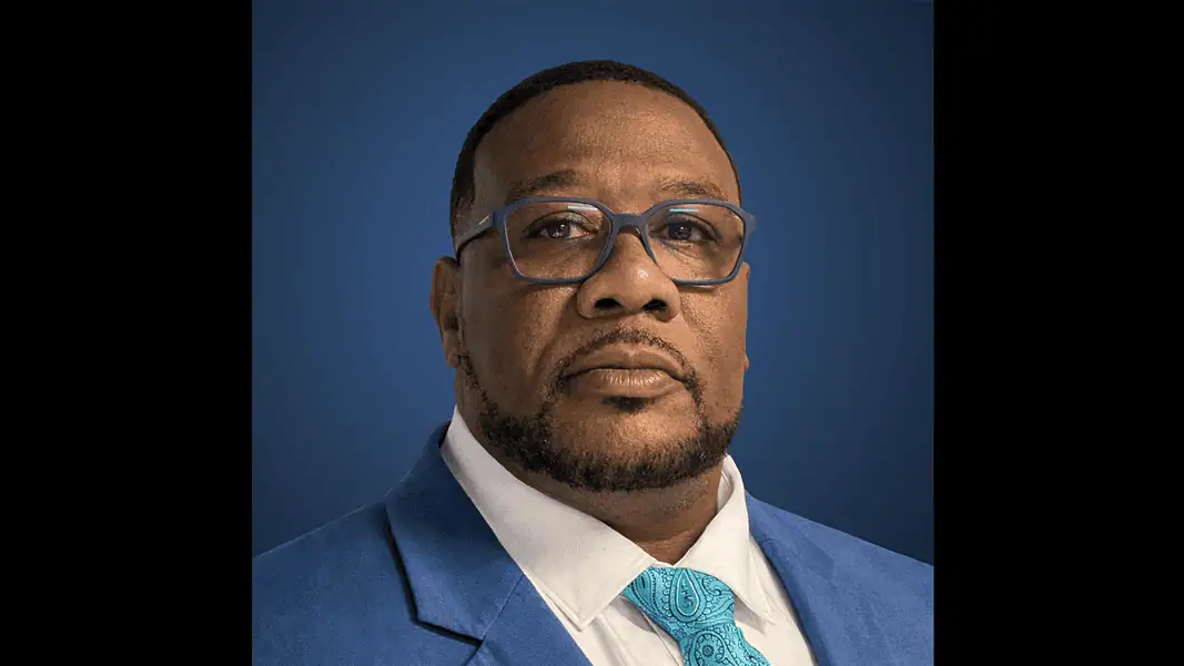 David Martin Metro Tech Portrait of a Black man in a blue suit, white shirt, and turquoise patterned tie, against a dark blue gradient background.