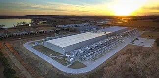 Aerial view of a large industrial warehouse complex at sunset, with rows of equipment along the side and a river nearby.