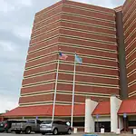 County cuts jail monitoring staff, meaning fewer eyes on detainees Tall red-brick building with beige horizontal bands, two flagpoles (American flag and blue flag) in front, and a parking lot with cars nearby.