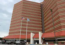 County cuts jail monitoring staff, meaning fewer eyes on detainees Tall red-brick building with beige horizontal bands, two flagpoles (American flag and blue flag) in front, and a parking lot with cars nearby.