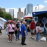 Festival of the Arts kicks off 60th year celebrating art in OKC People walk through an outdoor street fair with white tents and vendors, city skyscrapers in the background.