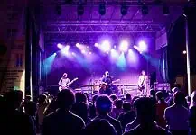 Norman Music Fest defined by feeling, haze, cross-genre range in 2026 Band performs on a lit stage with purple and blue lights as a crowd watches from the foreground at a nighttime concert.