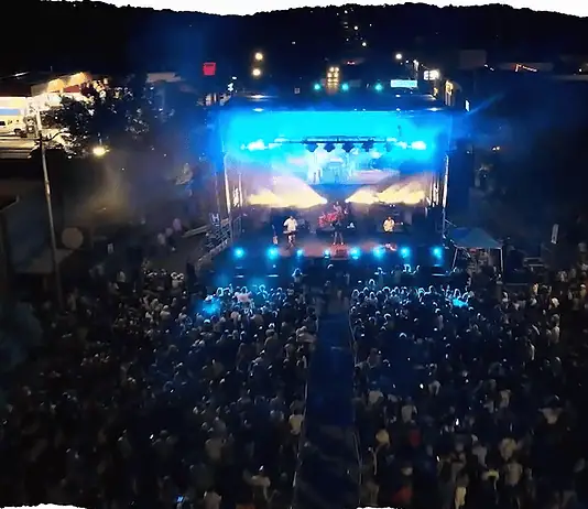 Here’s your guide to the can’t-miss acts at Norman Music Fest 2026 Aerial view of a nighttime outdoor concert with a large crowd facing a brightly lit stage and blue stage lights.