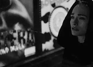 Dark thrillers, artsy horrors sink their teeth into OKC theaters Woman in a dark hooded coat stands in a dim urban street at night, looking worried or sad.