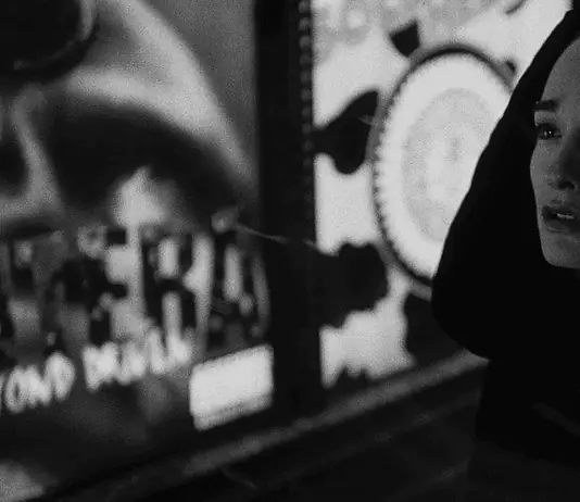 Dark thrillers, artsy horrors sink their teeth into OKC theaters Woman in a dark hooded coat stands in a dim urban street at night, looking worried or sad.