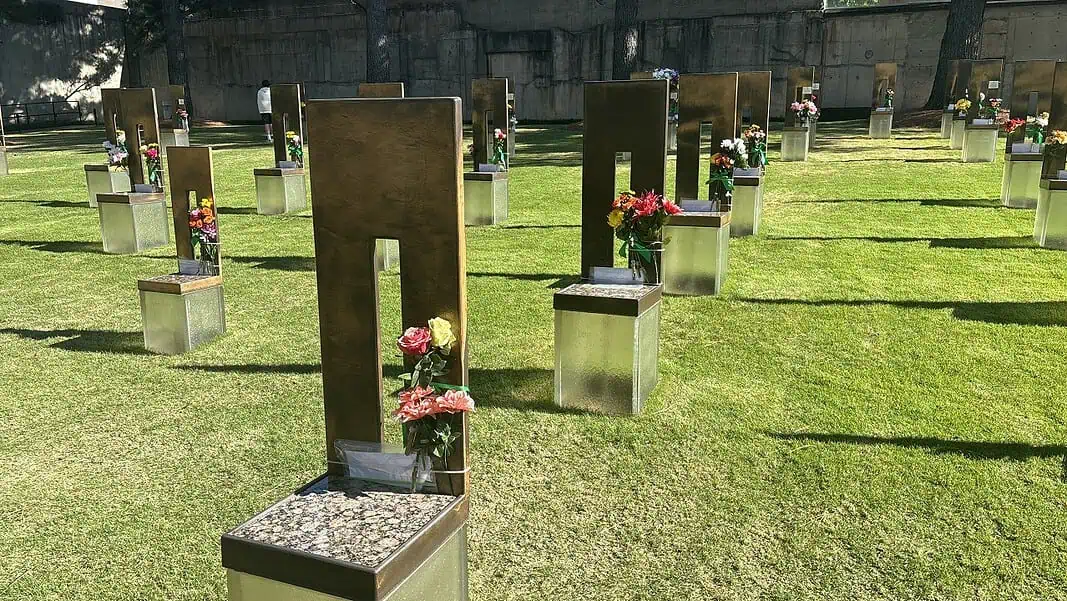 Photo Apr 18 2026, 5 18 15 PM Rows of bronze and metal grave markers with colorful flowers on a well-kept grassy cemetery lawn.