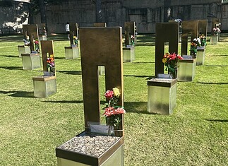 Rows of bronze and metal grave markers with colorful flowers on a well-kept grassy cemetery lawn.
