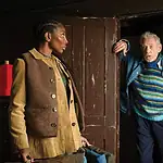 Soderbergh’s ‘The Christophers’ a two-handed rumination on art, legacy A young woman in a tan corduroy jacket stands in a room while an older man in a striped sweater steps through a dark doorway, gesturing with one hand.