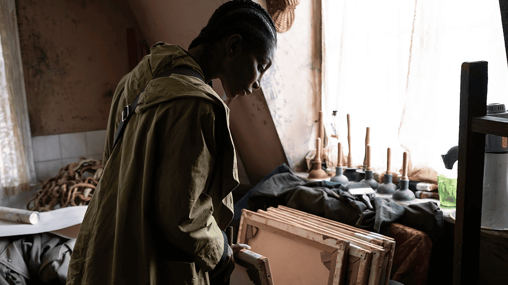 Person in an olive jacket examines wooden frames in a dim workshop.