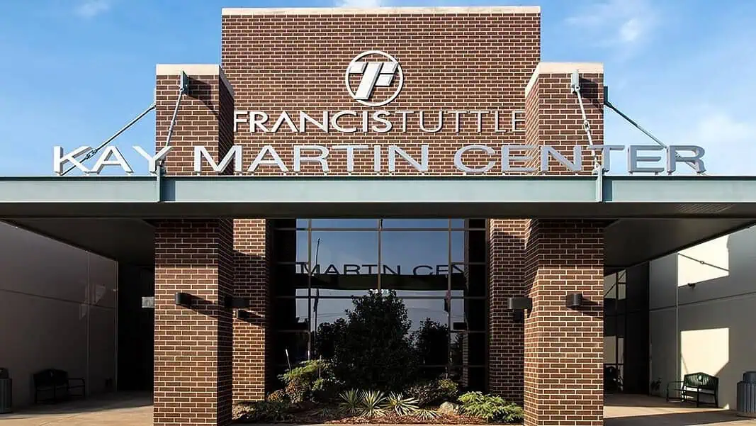 el_reno_campus-header_1900x660 Entrance to Francis Institute Kay Martin Center: brick façade, glass doors, and landscaped planters under a clear blue sky.