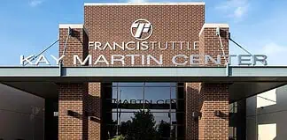 Entrance to Francis Institute Kay Martin Center: brick façade, glass doors, and landscaped planters under a clear blue sky.