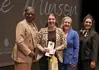 PRESS RELEASE: Karlie Minson named 2026 OKCPS District Teacher of the Year Four women in business attire on a stage; one woman in leopard print holds an award and a gift bag, flanked by three others celebrating.