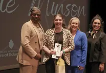 PRESS RELEASE: Karlie Minson named 2026 OKCPS District Teacher of the Year Four women in business attire on a stage; one woman in leopard print holds an award and a gift bag, flanked by three others celebrating.