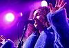 Love is in the spring air with songs of intensity, obsession, regret Female singer singing into a microphone on a concert stage under purple lights, wearing a blue fluffy coat