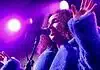 Love is in the spring air with songs of intensity, obsession, regret Female singer singing into a microphone on a concert stage under purple lights, wearing a blue fluffy coat