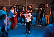 Color of Art returns to showcase diversity of OKC art, dance, music Group of youths forming a circle around a dancer in a white shirt performing a breakdance move under blue lighting.