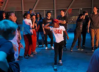Color of Art returns to showcase diversity of OKC art, dance, music Group of youths forming a circle around a dancer in a white shirt performing a breakdance move under blue lighting.