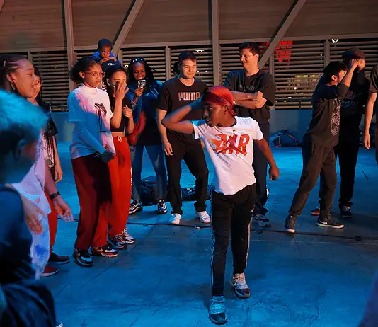 Color of Art returns to showcase diversity of OKC art, dance, music Group of youths forming a circle around a dancer in a white shirt performing a breakdance move under blue lighting.