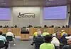 Business as usual at first Edmond City Council meeting since shooting City council chamber with a long wooden dais, officials seated, and a large Edmond logo on the back wall. Two screens read 'Edmond' on the sides. Audience seated in front.