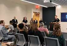 Lake Arcadia mass shooting victim dies; police provide few new answers Police officer at a podium addressing a seated audience in a briefing room, Edmond Police logo on a screen behind him.