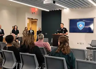Lake Arcadia mass shooting victim dies; police provide few new answers Police officer at a podium addressing a seated audience in a briefing room, Edmond Police logo on a screen behind him.