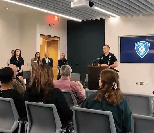 Lake Arcadia mass shooting victim dies; police provide few new answers Police officer at a podium addressing a seated audience in a briefing room, Edmond Police logo on a screen behind him.
