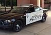 Two-tone Edmond Police patrol car (black and white) with a roof light bar, parked outside a brick building.