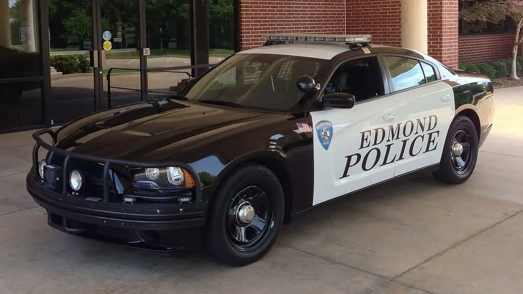 Edmond police vehicle (from policecarwebsite.net) Two-tone Edmond Police patrol car (black and white) with a roof light bar, parked outside a brick building.