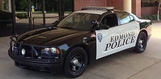 Two-tone Edmond Police patrol car (black and white) with a roof light bar, parked outside a brick building.