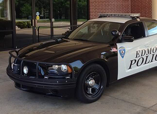 Two-tone Edmond Police patrol car (black and white) with a roof light bar, parked outside a brick building.