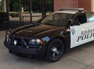 Suspect arrested in Arcadia Lake mass shooting; police chief speaks Two-tone Edmond Police patrol car (black and white) with a roof light bar, parked outside a brick building.