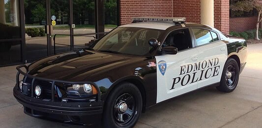 Two-tone Edmond Police patrol car (black and white) with a roof light bar, parked outside a brick building.