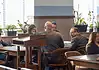 Judge moves Epic Charter Schools embezzlement case forward Formal meeting in a boardroom: people seated around a wooden table, a podium in the foreground, plants by the window.