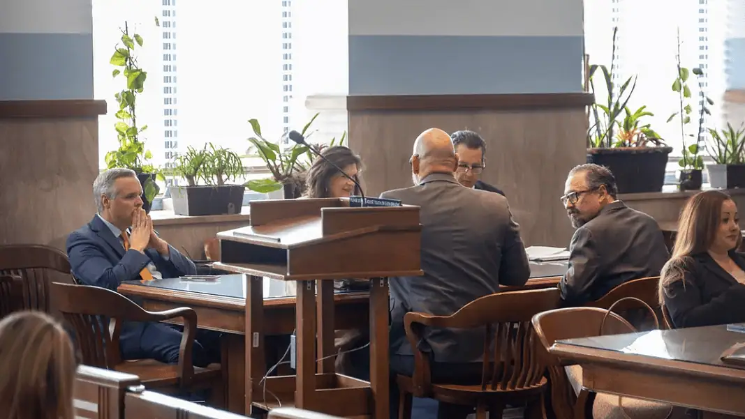 Epic founders in court Formal meeting in a boardroom: people seated around a wooden table, a podium in the foreground, plants by the window.