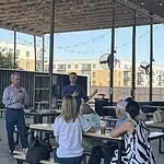 Edmond official says City not investigating police response to shooting A man in a blue sweater speaks to a small audience seated at picnic tables under an outdoor pavilion, with apartment buildings in the background.