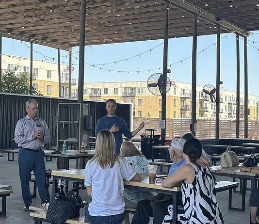 Edmond official says City not investigating police response to shooting A man in a blue sweater speaks to a small audience seated at picnic tables under an outdoor pavilion, with apartment buildings in the background.