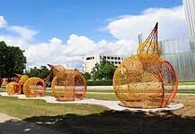 Massive ‘Formless Matter’ sculpture transforms OK Contemporary art park Outdoor art installation featuring large orange wire pumpkins on a curved concrete path in a park under a bright blue sky with white clouds.