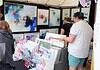 Art market stall with vivid abstract paintings on the walls and a display of cards and prints; shoppers browse the artwork.