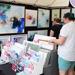 Paseo Arts Fest kicks off for a vibrant festival weekend Art market stall with vivid abstract paintings on the walls and a display of cards and prints; shoppers browse the artwork.