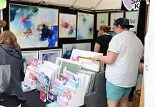 Paseo Arts Fest kicks off for a vibrant festival weekend Art market stall with vivid abstract paintings on the walls and a display of cards and prints; shoppers browse the artwork.