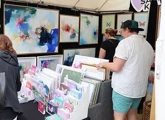 Paseo Arts Fest kicks off for a vibrant festival weekend Art market stall with vivid abstract paintings on the walls and a display of cards and prints; shoppers browse the artwork.