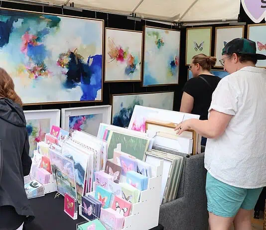 Paseo Arts Fest kicks off for a vibrant festival weekend Art market stall with vivid abstract paintings on the walls and a display of cards and prints; shoppers browse the artwork.