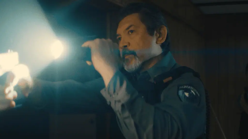 Male officer in uniform shines a flashlight into a dim room, beam across the scene,