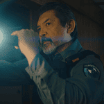 Male officer in uniform shines a flashlight into a dim room, beam across the scene,