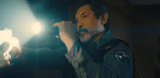Male officer in uniform shines a flashlight into a dim room, beam across the scene,