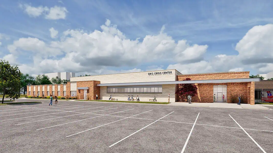 MAPS 4 Mental Health Crisis enter Exterior view of the OKC Crisis Center with a brick and tan facade and a spacious parking lot in the foreground, daytime with people walking nearby.